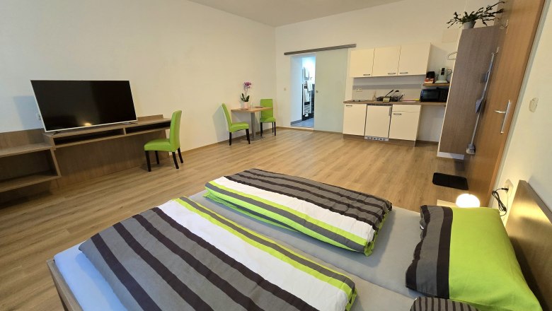 Modern apartment with double bed, TV, dining table and kitchenette.