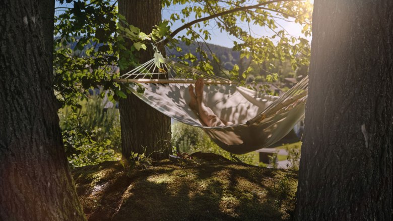 Person entspannt in einer Hängematte zwischen zwei Bäumen im Wald.