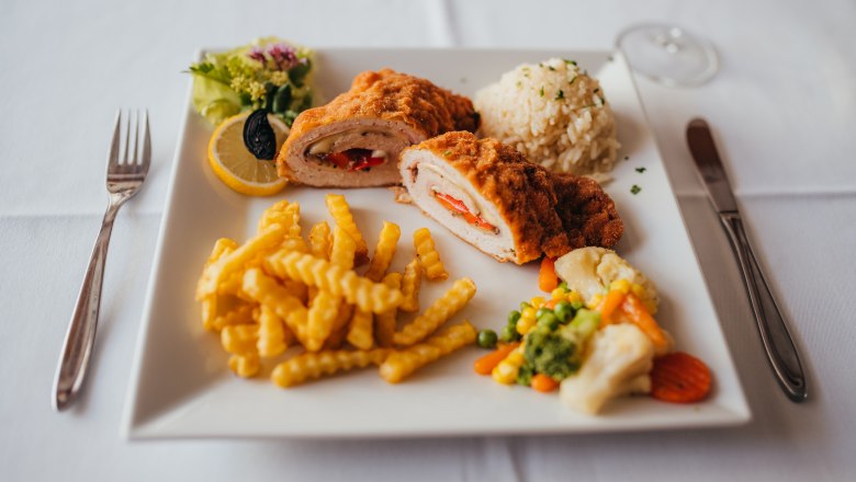 Gebackenes Hähnchen mit Pommes, Reis und Gemüse auf weißem Teller.