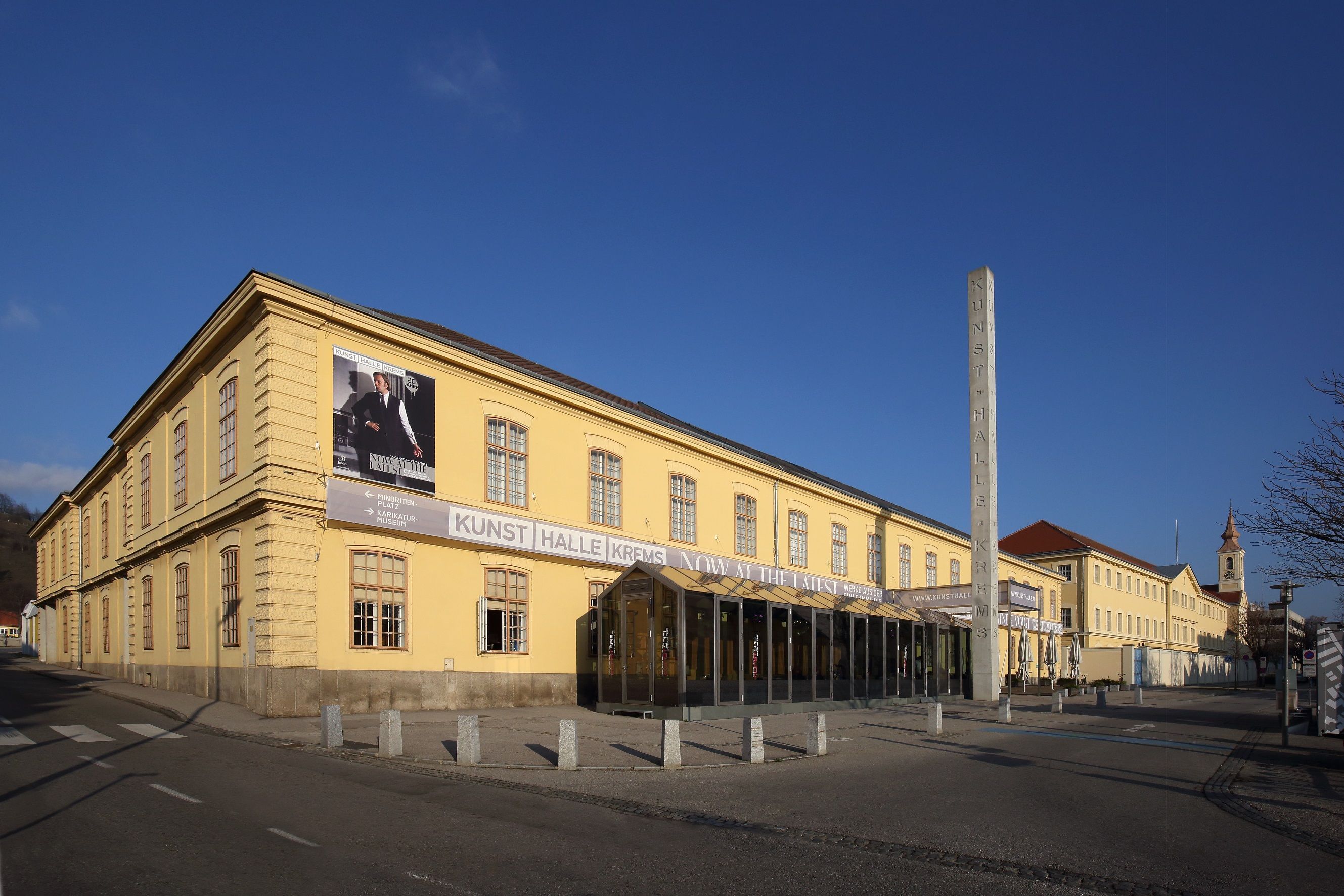 Außenansicht der Kunsthalle Krems mit gelbem Gebäude und blauem Himmel.