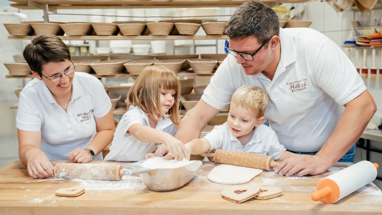 Familie beim Backen in einer Bäckerei mit vielen Brotkörben im Hintergrund.