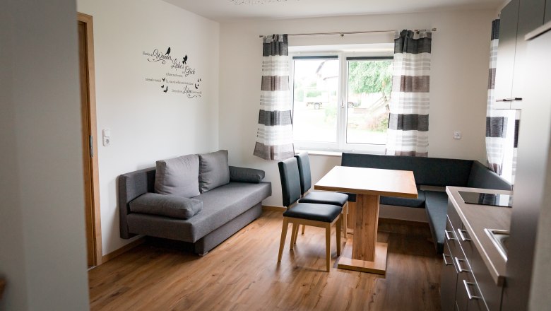 Moderne Küche mit grauem Sofa, Holztisch und Stühlen, Fenster mit Vorhängen.