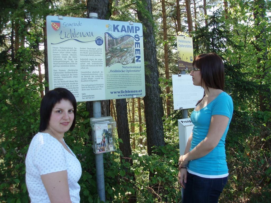 Zwei Frauen stehen vor einem Schild mit der Aufschrift 'Naturdenkmal Heidnische Opferstätte' im Wald.