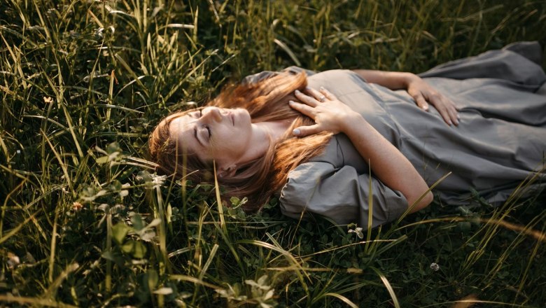 Frau liegt entspannt im Gras mit geschlossenen Augen und einer Hand auf der Brust.