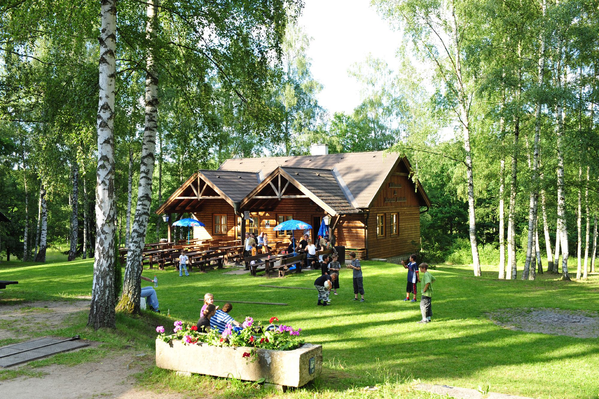 Holzhütte im Naturpark Blockheide mit spielenden Kindern und Bäumen.