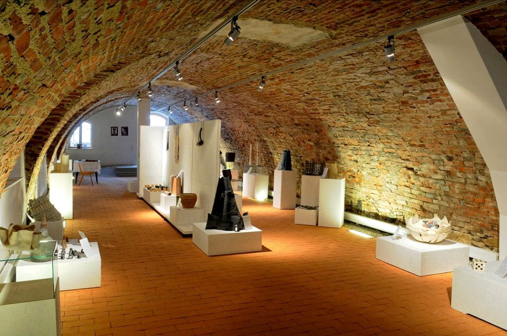 Ausstellungsraum mit Backsteinwänden und Kunstwerken auf Podesten.