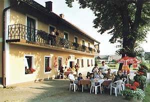 Ein Gasthof mit Terrasse, auf der Menschen an Tischen sitzen, umgeben von Sonnenschirmen und Blumen.
