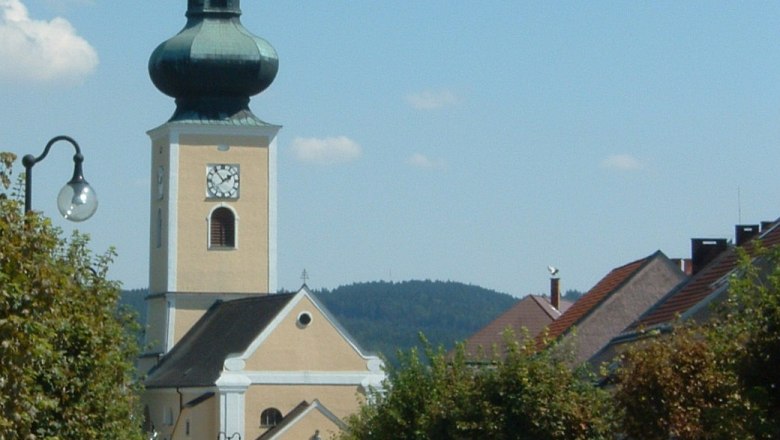 Kirche mit Zwiebelturm in einer kleinen Stadt, umgeben von Bäumen und Häusern.