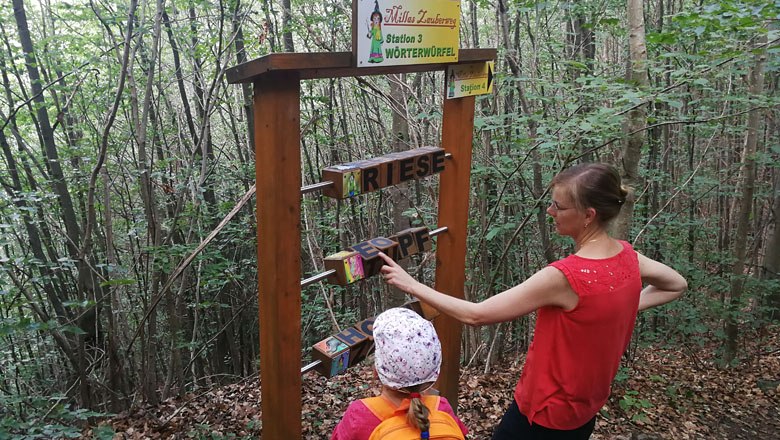 Zwei Personen an einer Station im Wald mit Wortw&uuml;rfeln auf Millas Zauberweg.