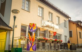 Exterior view of a café with terrace and colorful floral decorations.