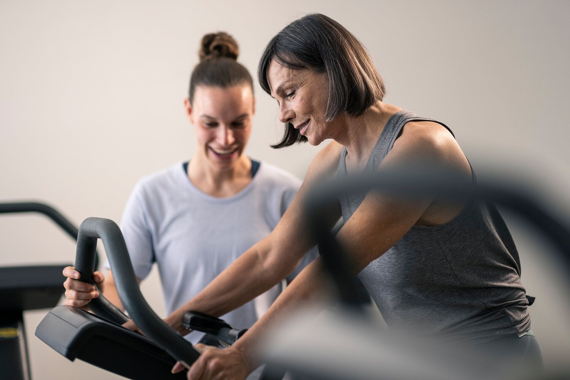Eine Therapeutin begleitet eine Frau beim Training auf einem Ergometer im Gesundheits- und Rehabilitationszentrum Moorheilbad Harbach im Waldviertel. Beide wirken konzentriert und freundlich.