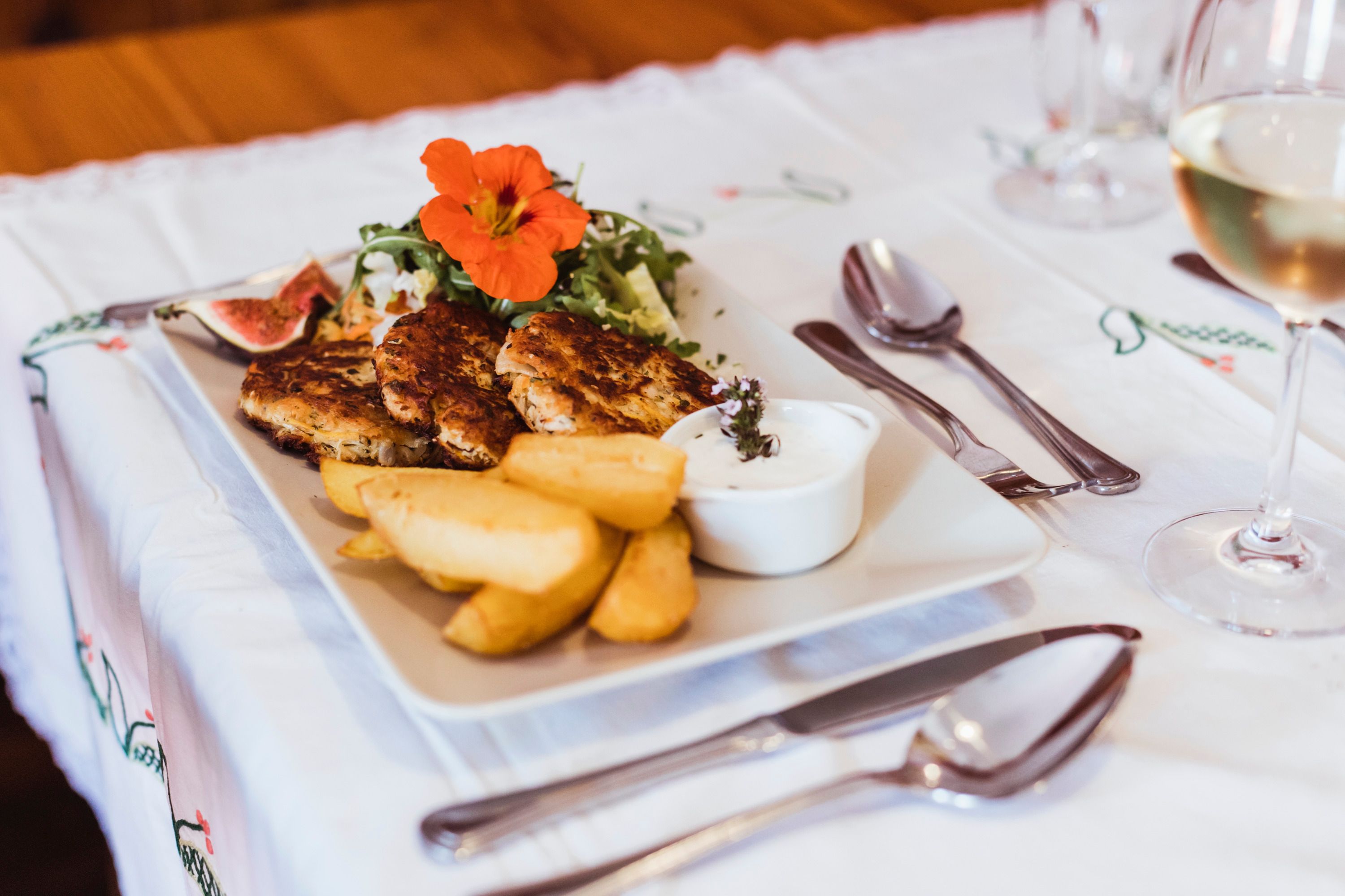 Ein Teller mit Vollkorn-Sauerkrautlaibchen, Kartoffelspalten, Salat und Dip auf einem Tisch.