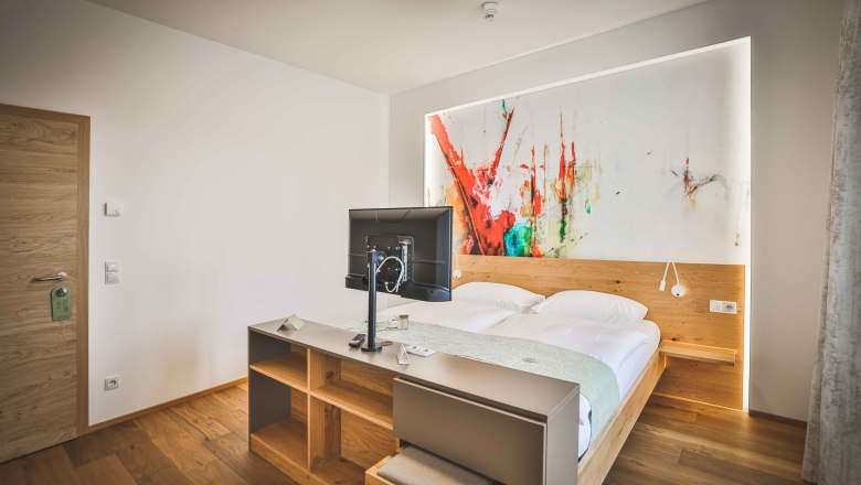 Modernes Hotelzimmer mit Doppelbett, abstraktem Kunstwerk an der Wand und Fernseher auf einem Tisch.
