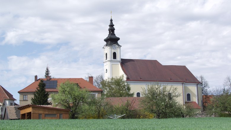 Kirche in Sankt Leonhard am Hornerwald mit umliegenden Gebäuden und grünem Feld.