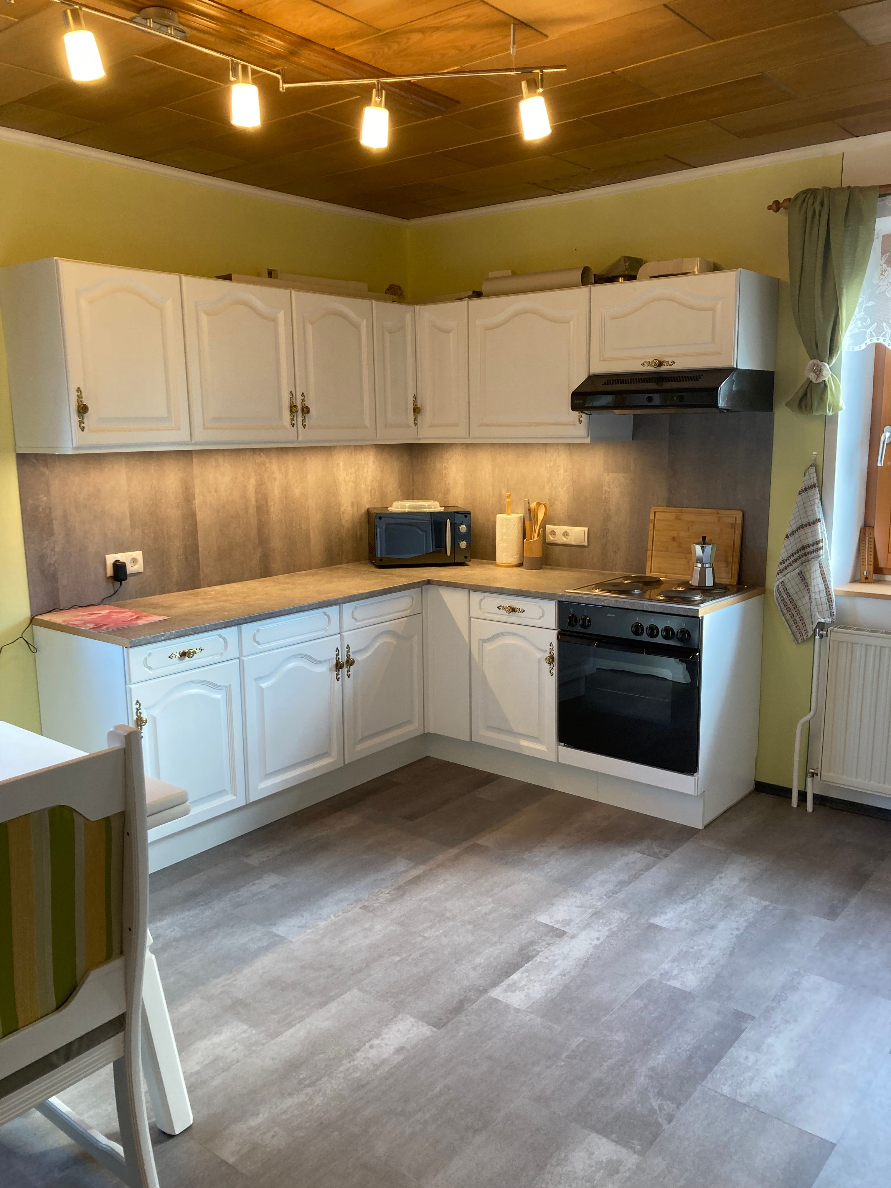 Geräumige Küche mit weißen Schränken, Herd, Mikrowelle und Holzdecke.