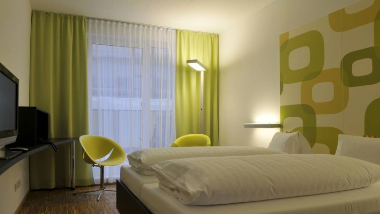 Modernes Hotelzimmer mit Doppelbett, grün-gelben Vorhängen und Wanddekor.