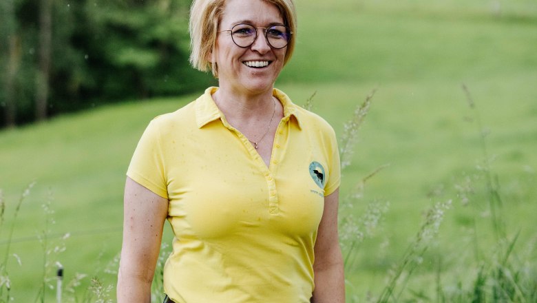 The owner, Sandra Anderl, stands smiling on a green meadow.
