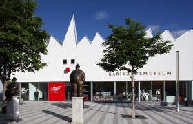 Außenansicht des Karikaturmuseums Krems mit Statuen und Bäumen.