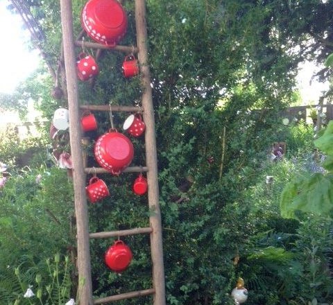 Eine Holzleiter im Garten, behängt mit roten Töpfen und Tassen mit weißen Punkten.