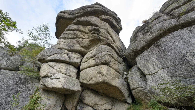 Großer Felsblock mit Schichtungen in Bad Traunstein, umgeben von Bäumen und Himmel.
