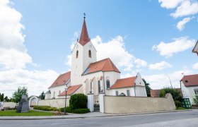 Kirche in Schweiggers mit rotem Dach und Turm vor blauem Himmel.