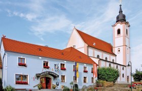 Gasthaus Gamerith neben einer Kirche mit Turm und rotem Dach.