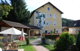 Gelbes Gebäude mit Wandgemälde, Garten mit Sonnenschirm und Sitzbereich.