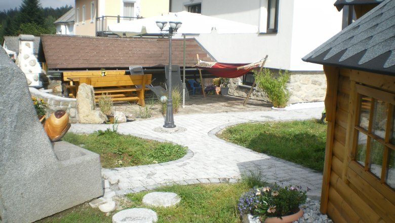 Garten mit Steinen, Holzhaus, Tisch, Hängematte und Sonnenschirm.