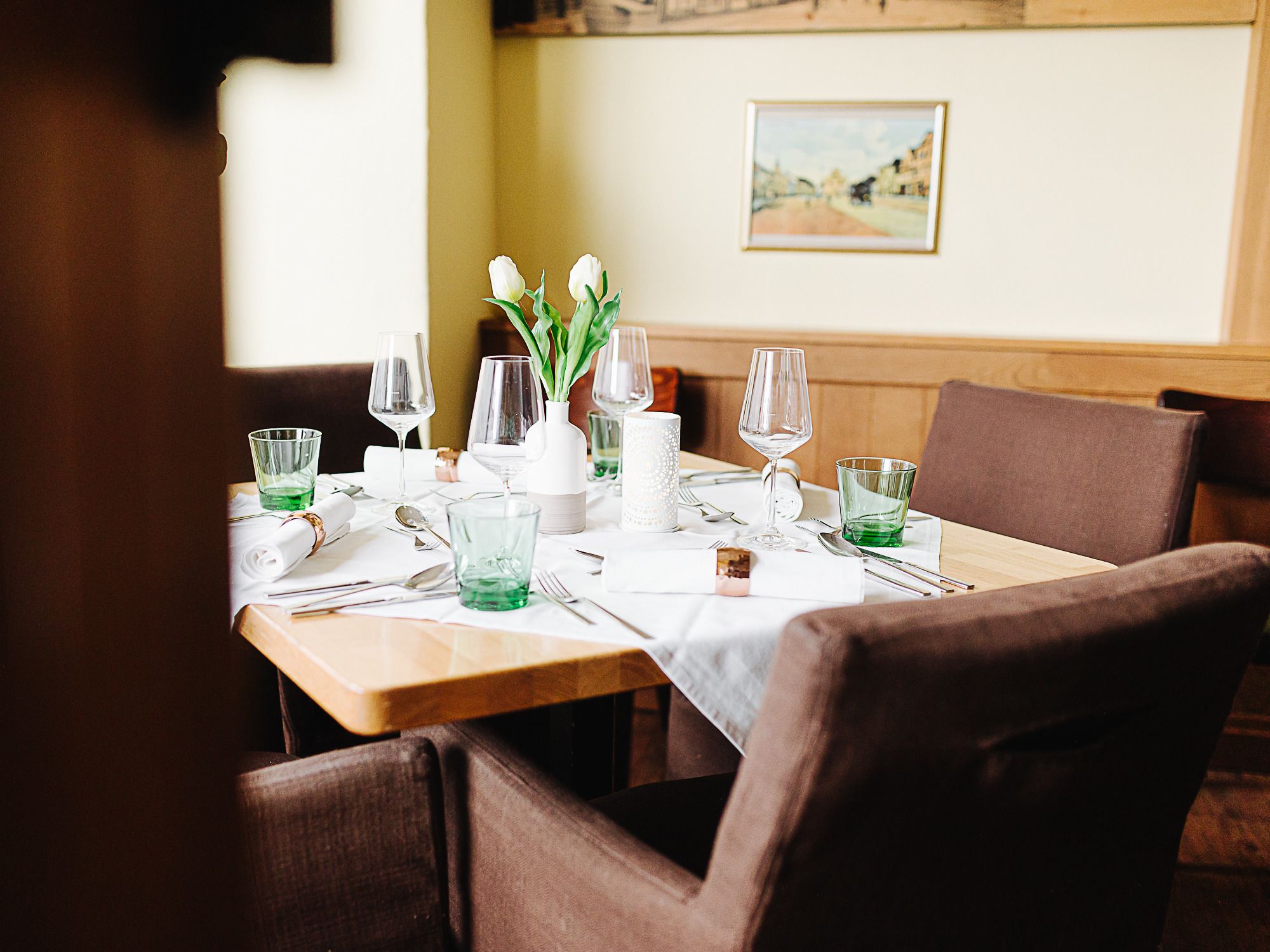 Ein elegant gedeckter Tisch in einem Gasthaus mit Gläsern, Besteck und weißen Tulpen in einer Vase.
