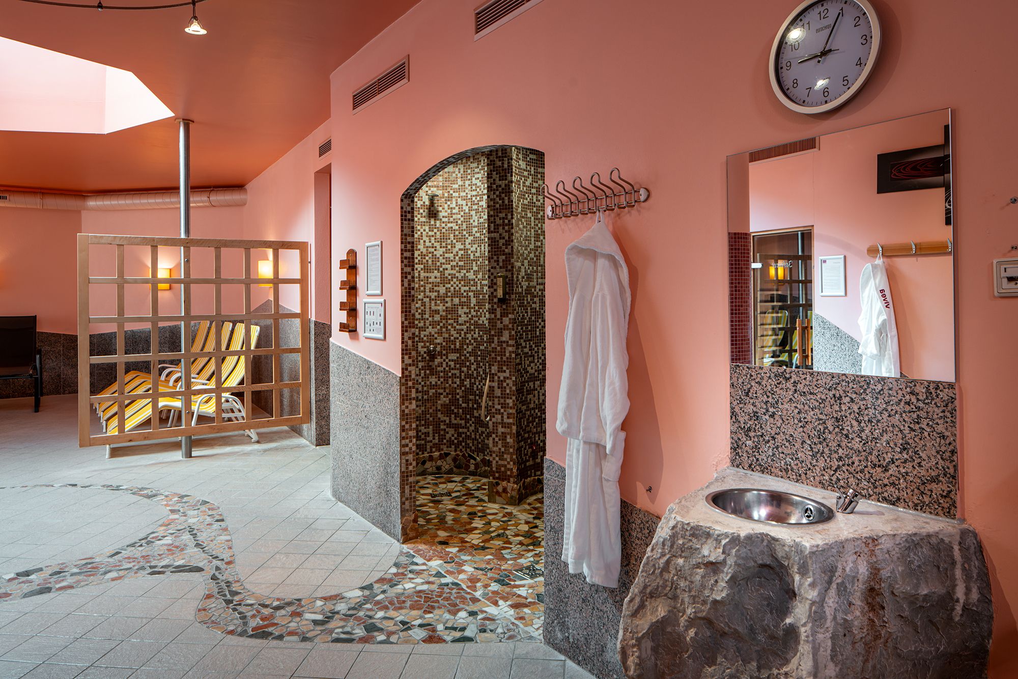 Innenansicht eines Wellnessbereichs mit Sauna, Liegestühlen und Waschbecken.