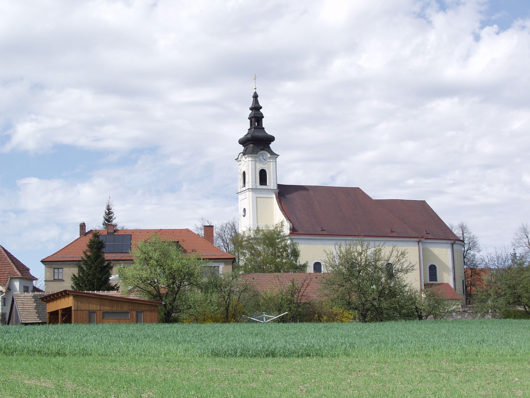 Kirche in Sankt Leonhard am Hornerwald mit umliegenden Gebäuden und grünem Feld.