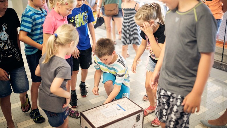 Children stand around a treasure chest lying on the floor.