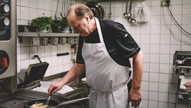 A cook in a professional kitchen is frying something in a pan.