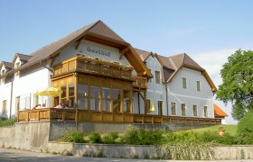 Ein traditioneller Gasthof mit Holzveranda und Blumen auf dem Balkon, umgeben von grüner Landschaft.