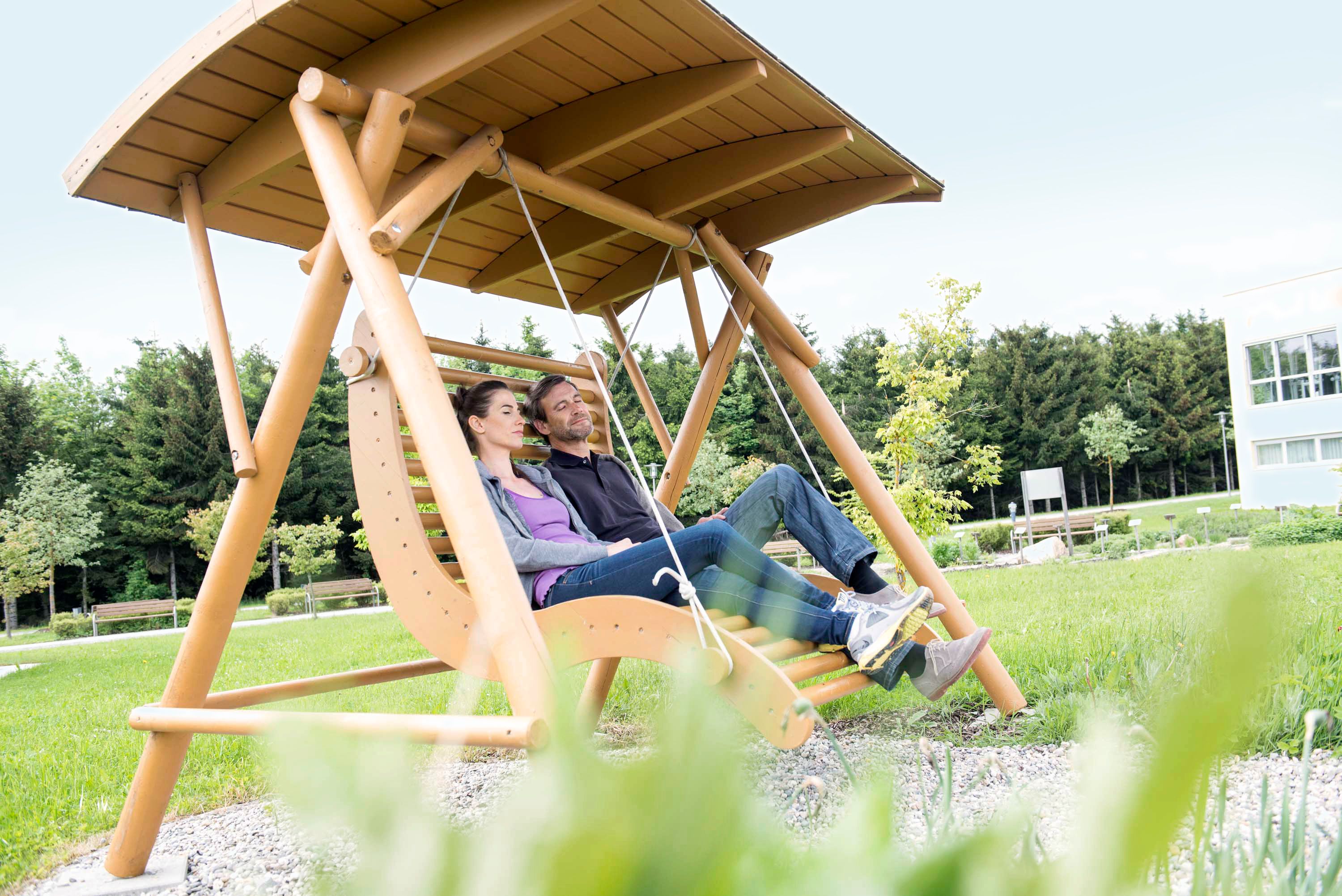 Ein Paar entspannt auf einer großen Holzschaukel im Freien.