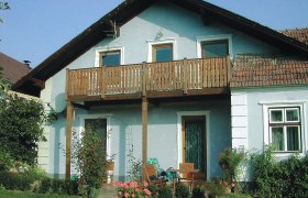 Ein traditionelles Winzerhaus mit Holzbalkon und Gartenmöbeln vor der Tür.