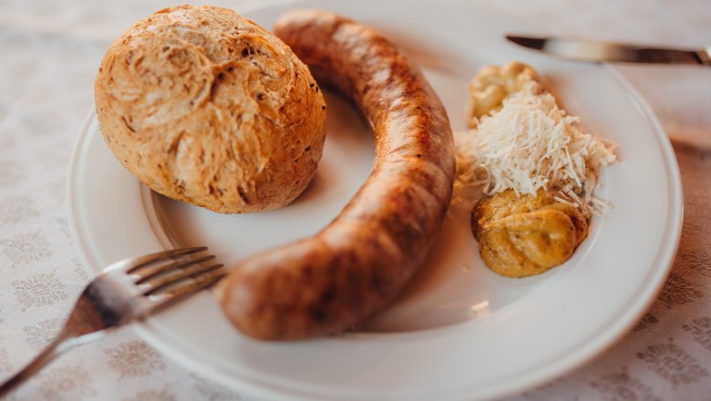 Ein Teller mit einer Bratwurst, einem Brötchen, Senf und geriebenem Meerrettich.