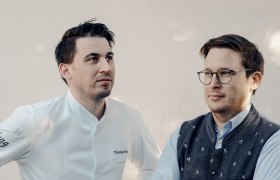 Zwei Männer stehen nebeneinander, einer in Kochjacke, der andere in Trachtenweste.