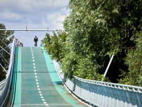 Die sanfte Erhebung der Radwegbr&uuml;cke l&auml;dt Radfahrer ein, die malerische Landschaft zu erkunden. Umgeben von &uuml;ppigem Gr&uuml;n und dem sanften Rauschen der B&auml;ume, bietet dieser Ort eine perfekte Kulisse f&uuml;r unvergessliche Ausfl&uuml;ge in die Natur.