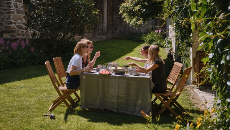 Vier Frauen sitzen an einem Tisch im Garten und genießen eine Mahlzeit.