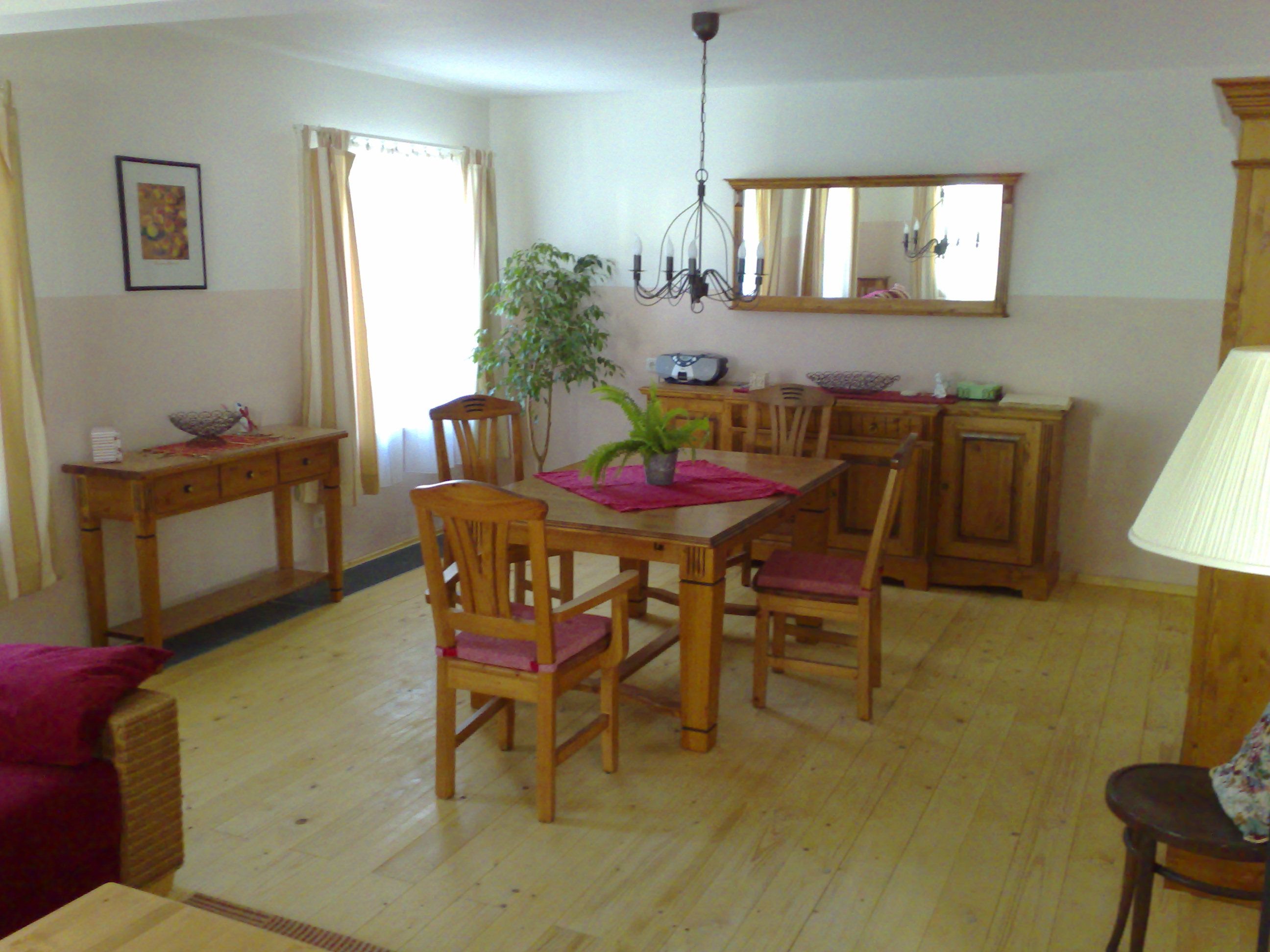 Gemütliches Wohnzimmer mit Holzmöbeln, Esstisch, Stühlen und Pflanzen.