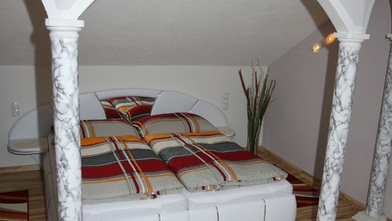 Schlafzimmer mit Doppelbett, Marmorsäulen und gestreifter Bettwäsche.