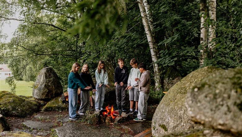 Gruppe von Jugendlichen steht um ein Lagerfeuer im Wald.