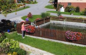 Ein gepflegter Garten mit Blumenbeeten und einem kleinen Teich in einem Dorf.