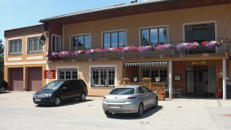 Gasthaus mit Balkon und Blumen, zwei geparkte Autos davor.