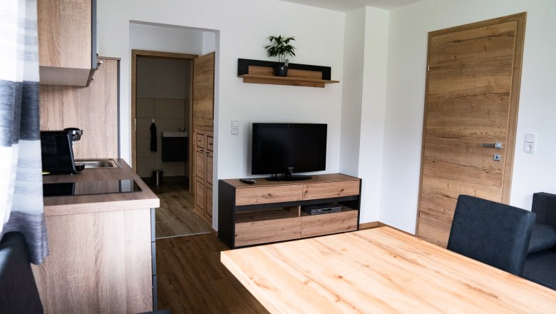 Modernes Wohnzimmer mit Holzmöbeln, Fernseher und Küche.