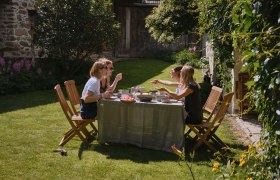 Vier Frauen sitzen an einem Tisch im Garten und genießen eine Mahlzeit.