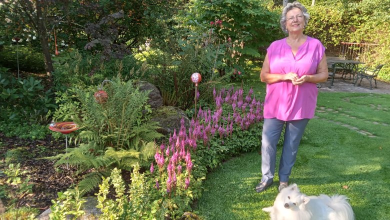 Eine Frau steht in einem Garten neben einem weißen Hund auf dem Rasen.