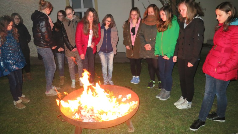 Gruppe von Jugendlichen steht um eine Feuerstelle im Freien.