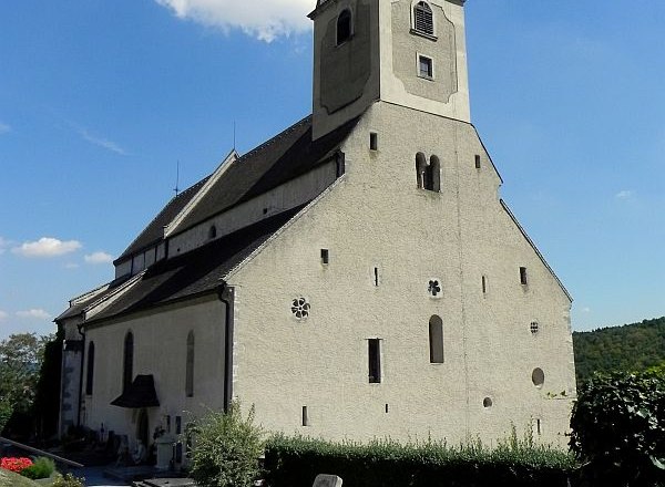 Eine historische Kirche mit einem Turm und umliegendem Friedhof bei klarem Himmel.